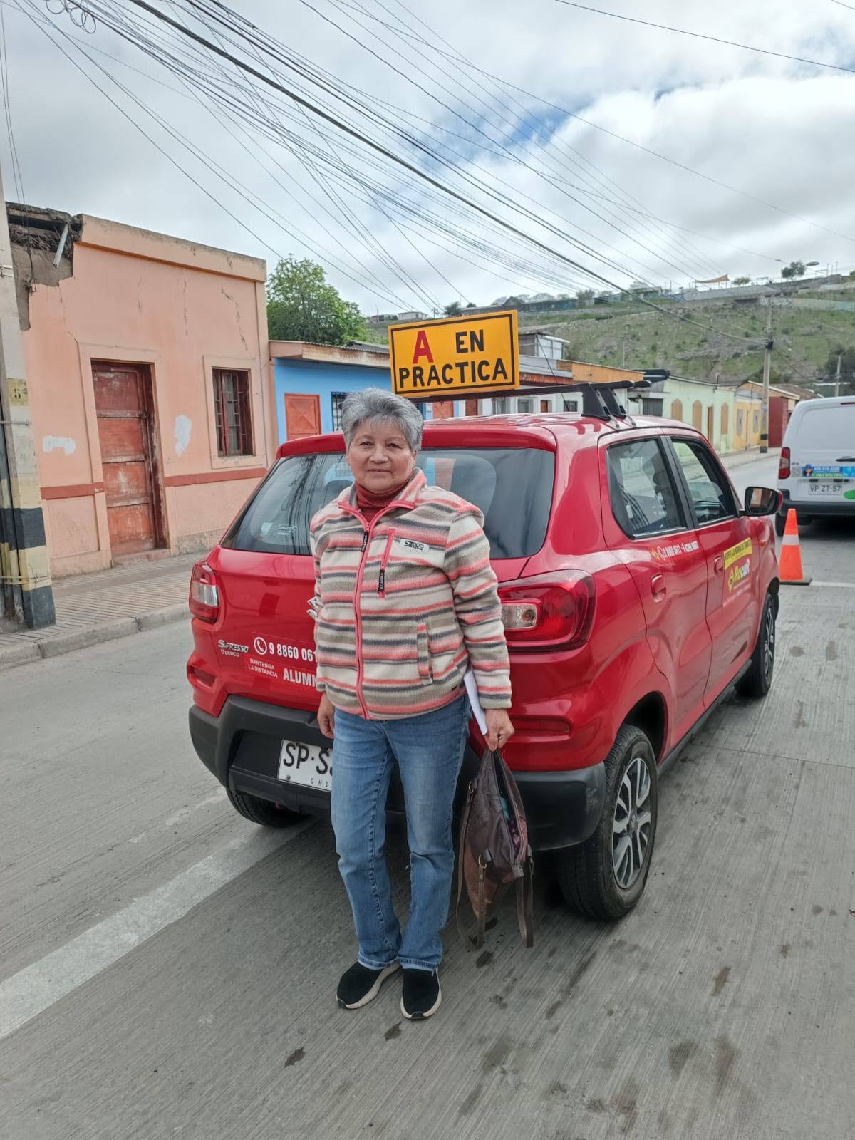 Alumna junto al auto rojo de la escuela con el cartel A en práctica, en Vallenar