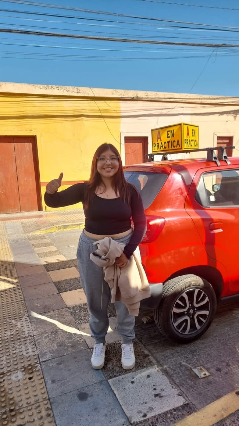 Alumna con el pulgar arriba junto al auto rojo de la escuela con el cartel A en práctica, en Vallenar