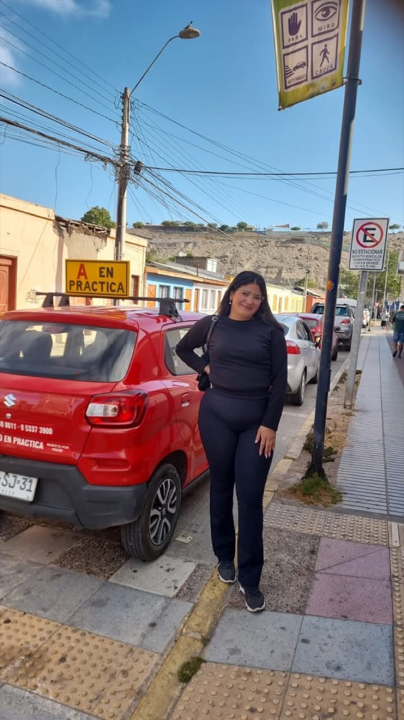 Alumna de pie junto al auto rojo de la escuela con el cartel A en práctica, en una calle de Vallenar