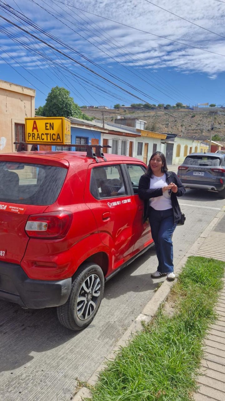 Alumna sonriendo junto al auto rojo de la escuela con el cartel A en práctica, en Vallenar