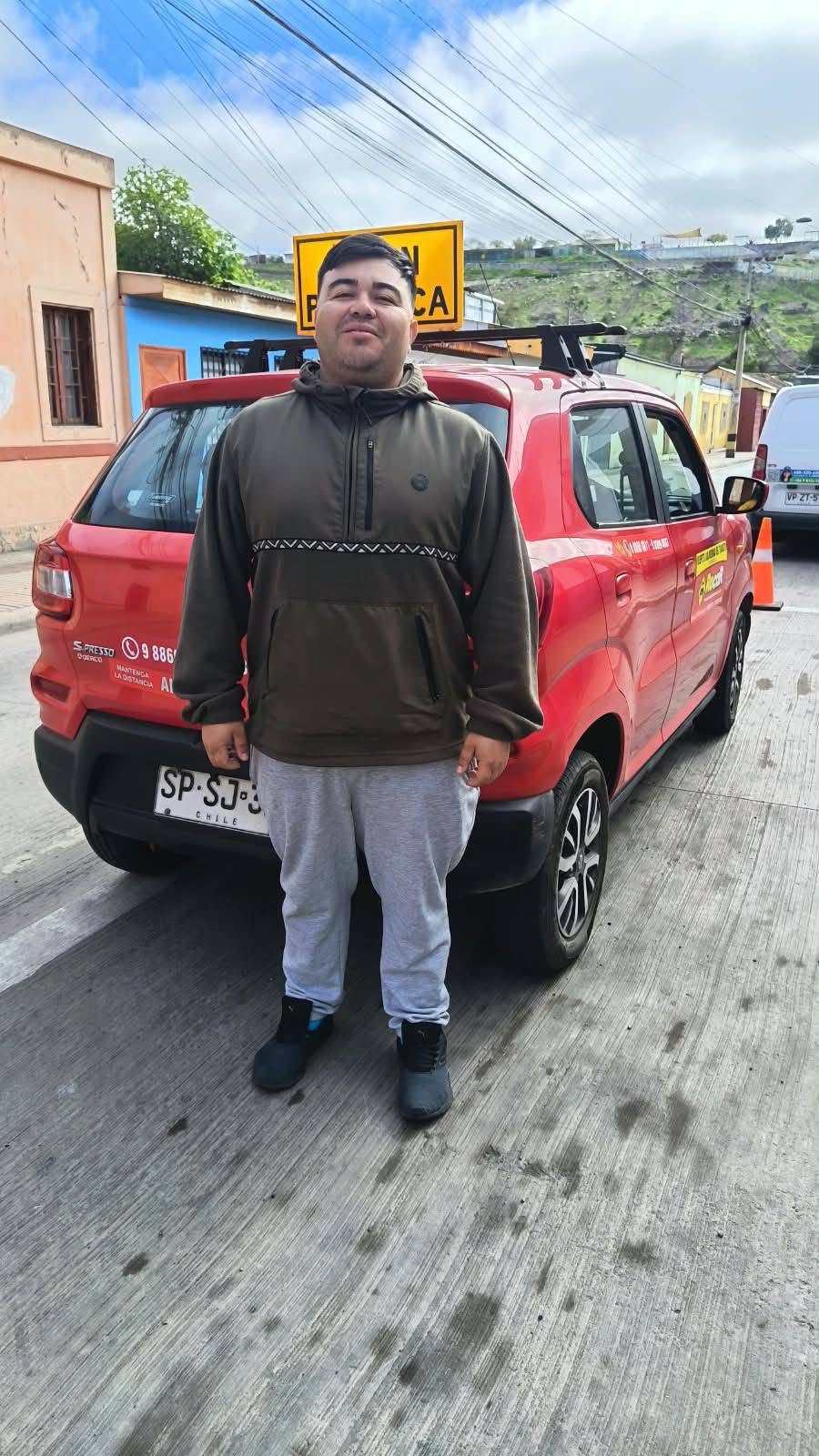 Alumno junto al auto rojo de la escuela con el cartel A en práctica, en Vallenar