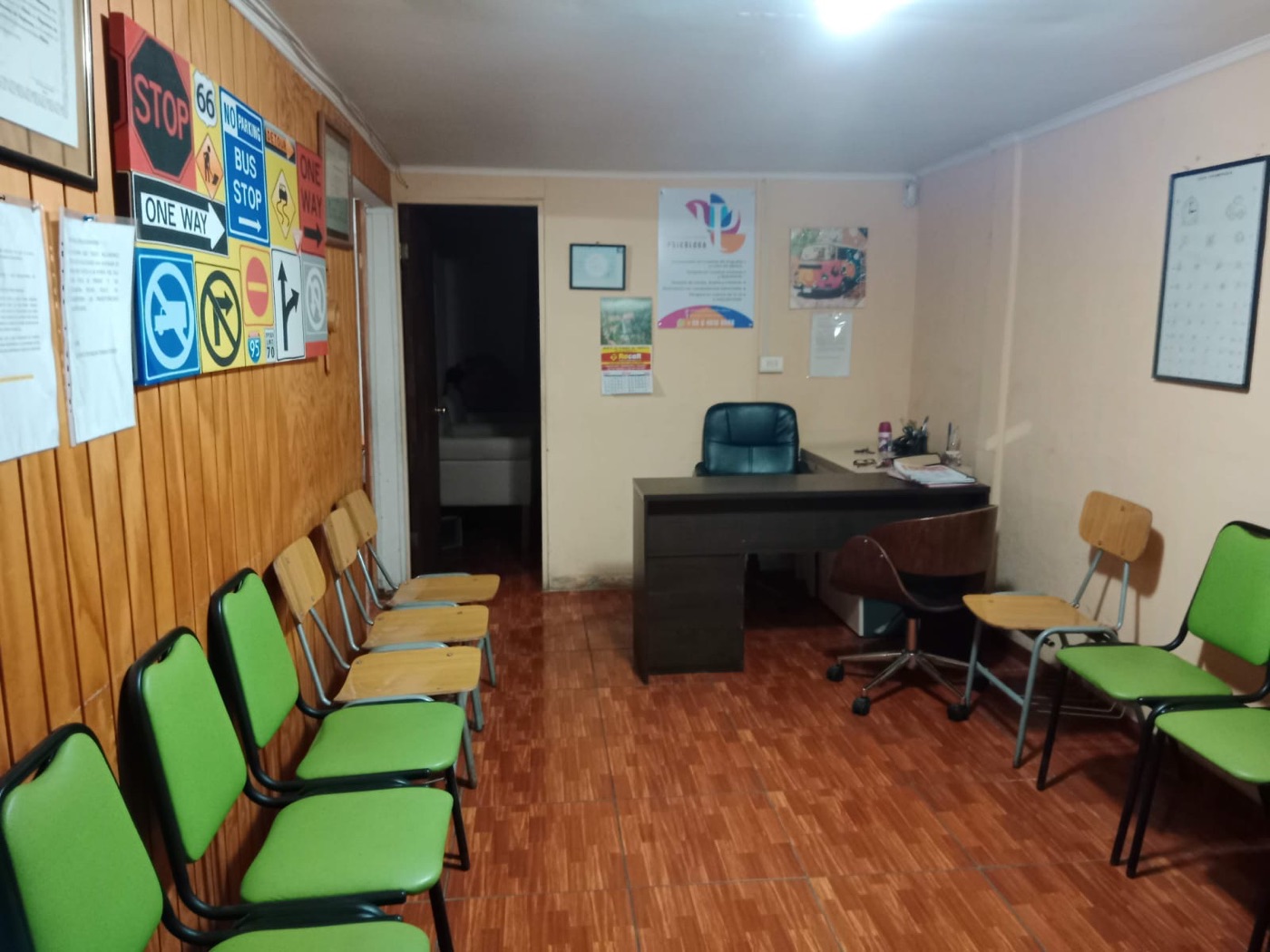 Sala de espera con sillas verdes, escritorio de atención y letreros de tránsito en la pared